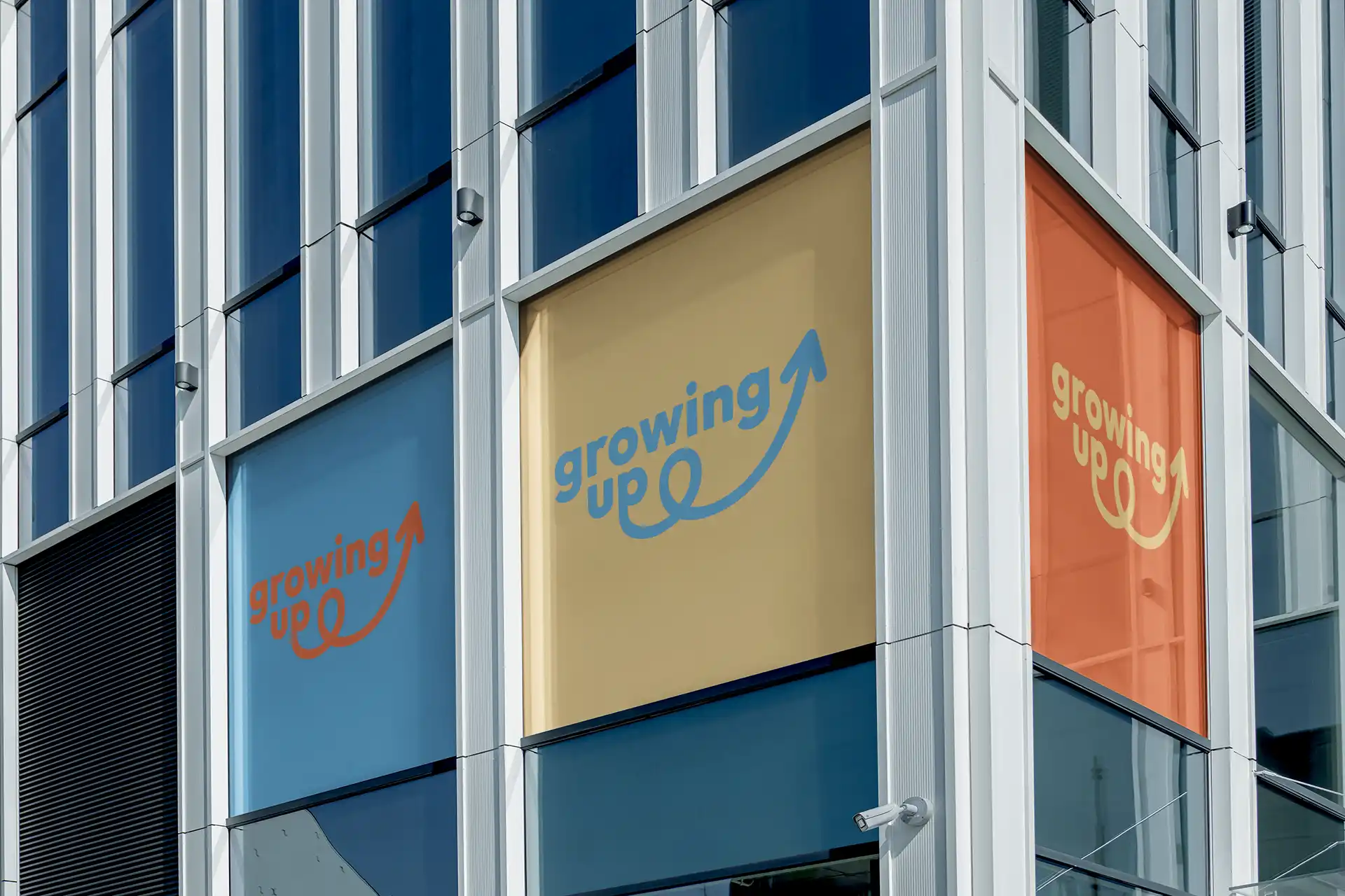 Logo Growing Up décliné en trois couleurs (bleu, doré, orange) sur les vitres d'un immeuble de bureaux