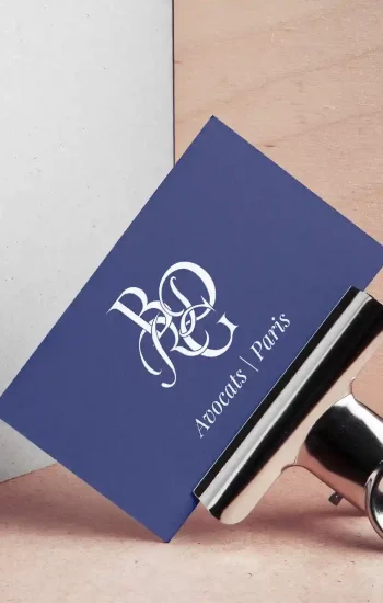 Carte de visite bleu marine du cabinet d'avocats BDRG Paris, monogramme calligraphié blanc, présentée sur fond bois et béton avec pince métallique