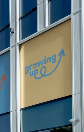 Logo Growing Up décliné en trois couleurs (bleu, doré, orange) sur les vitres d'un immeuble de bureaux