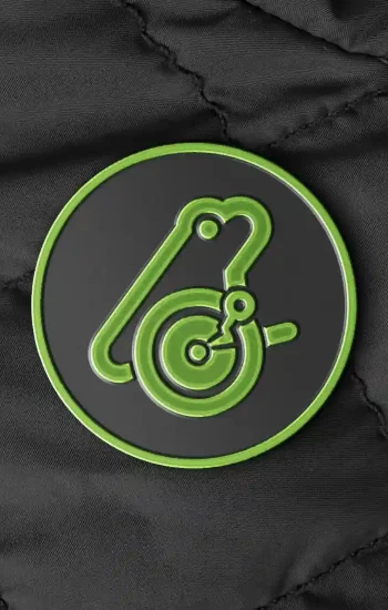Pin's émaillé rond édition limitée Froggo, logo grenouille stylisée vert néon sur fond noir, posé sur un blouson matelassé